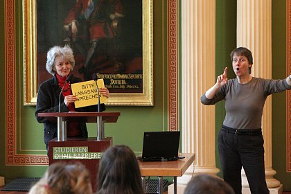 Prof. Dr. Christa Schlenker-Schulte von der FST (links) weist gleich zu Beginn darauf hin, dass auf langsames Sprechen geachtet werden soll (Gebrdensprachdolmetscherin: Heike Leps)